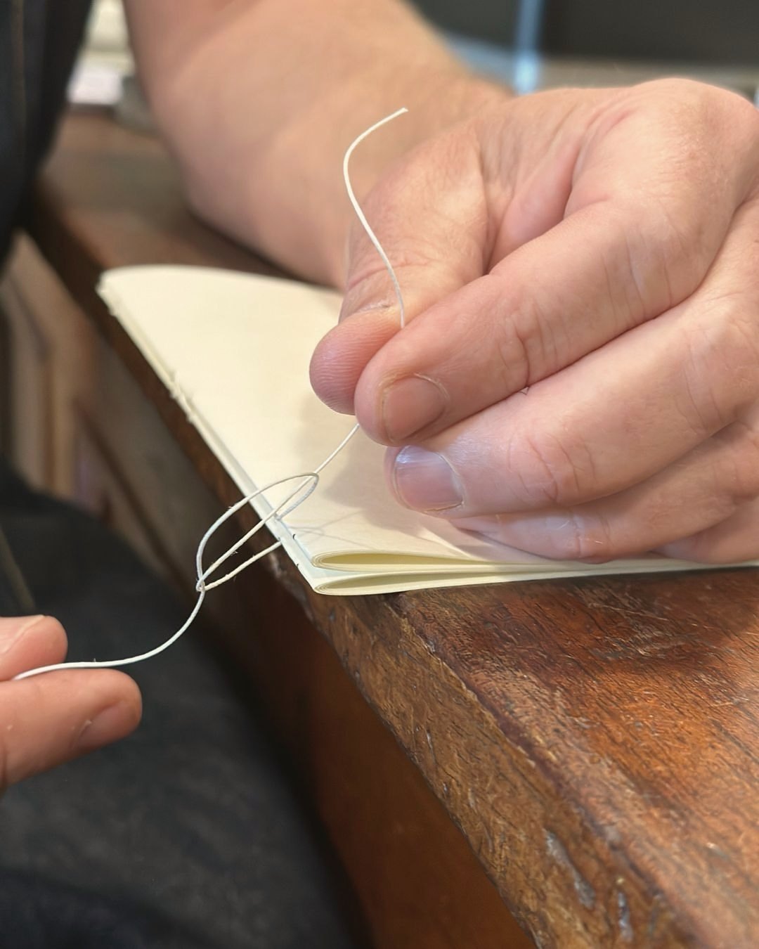 Hands sewing a notebook's signatures